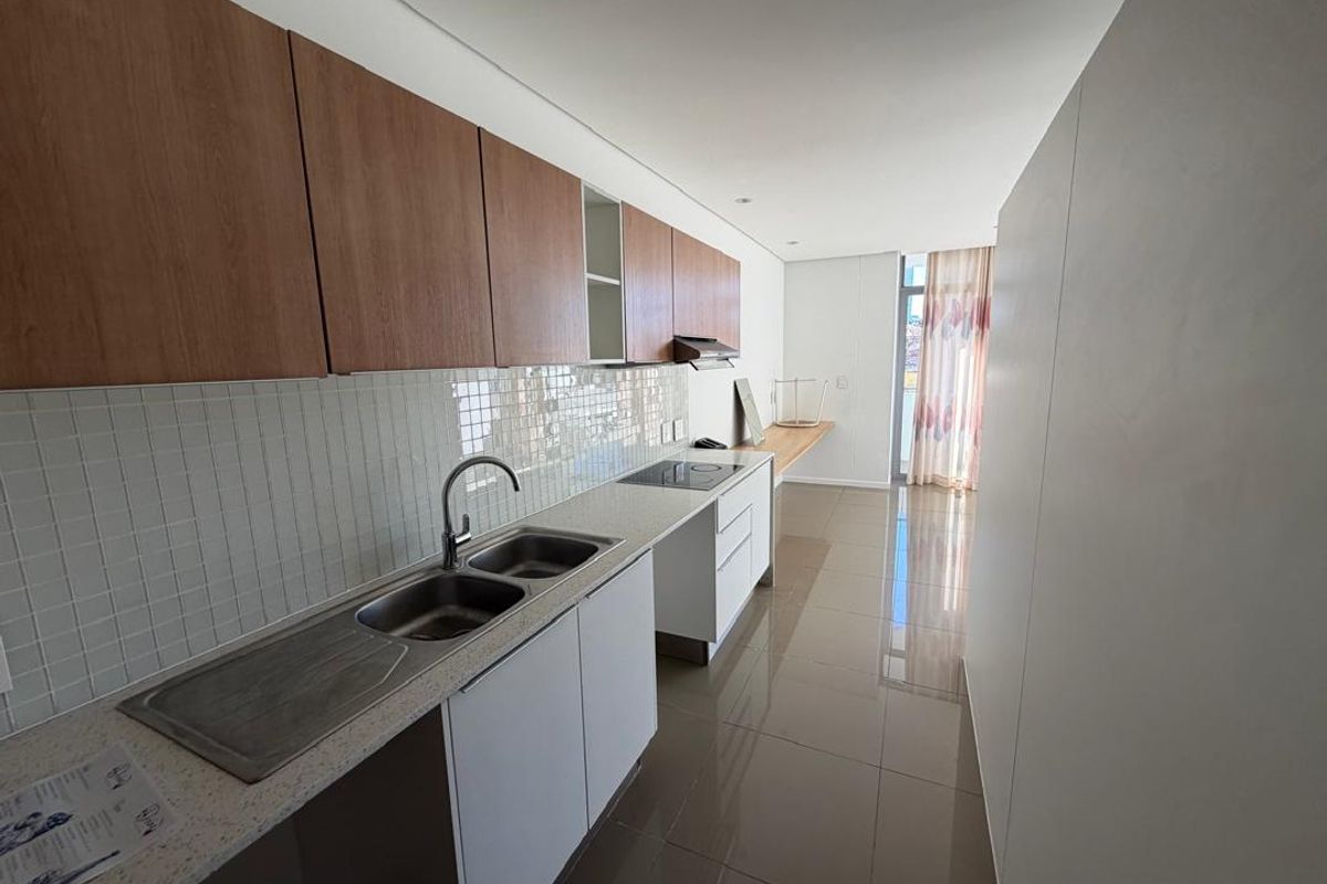 Modern galley-style kitchen featuring light wood-tone upper cabinets, white lower cabinetry, stone countertops, and integrated hob with extractor fan.