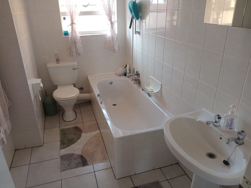 A functional bathroom featuring a standard bathtub, pedestal basin, and toilet with white wall tiling and tiled flooring throughout.