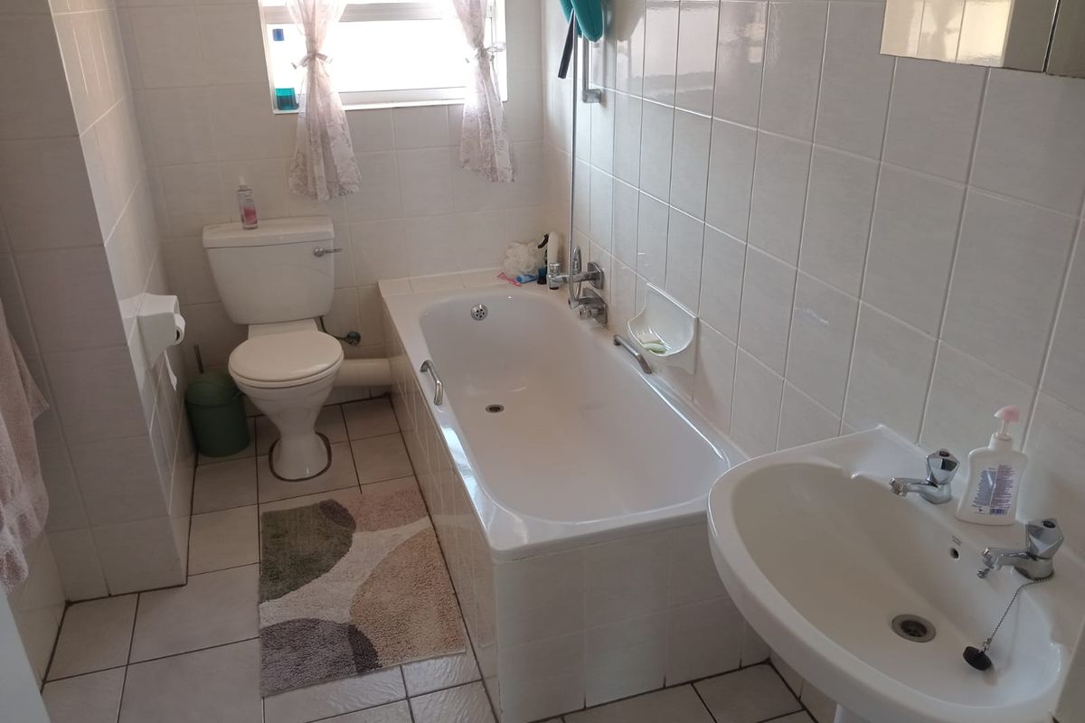 A functional bathroom featuring a standard bathtub, pedestal basin, and toilet with white wall tiling and tiled flooring throughout.