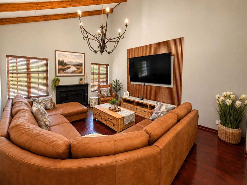 Spacious living room featuring a vaulted ceiling with exposed timber beams, a slatted wood feature wall, fireplace, and rich timber flooring.