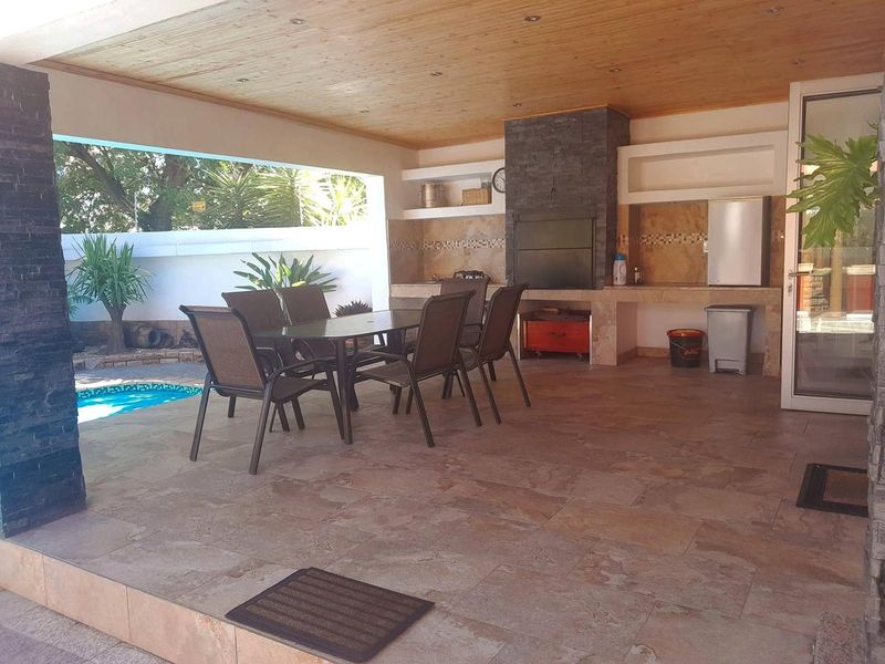 Spacious covered patio featuring a built-in braai, stone cladding, timber ceiling, and direct access to the pool area, perfect for outdoor entertaining.
