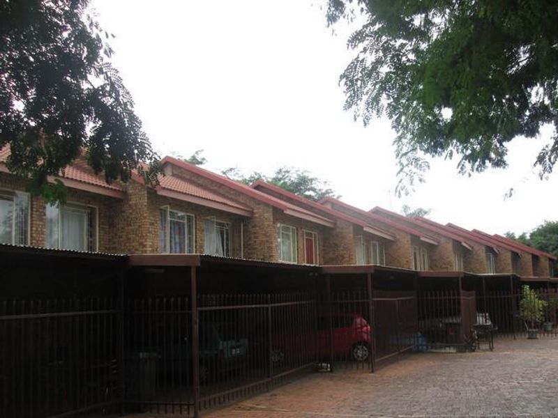 Exterior view of a residential apartment complex featuring a brick facade, tiled roofing, and a row of covered carports with metal fencing.