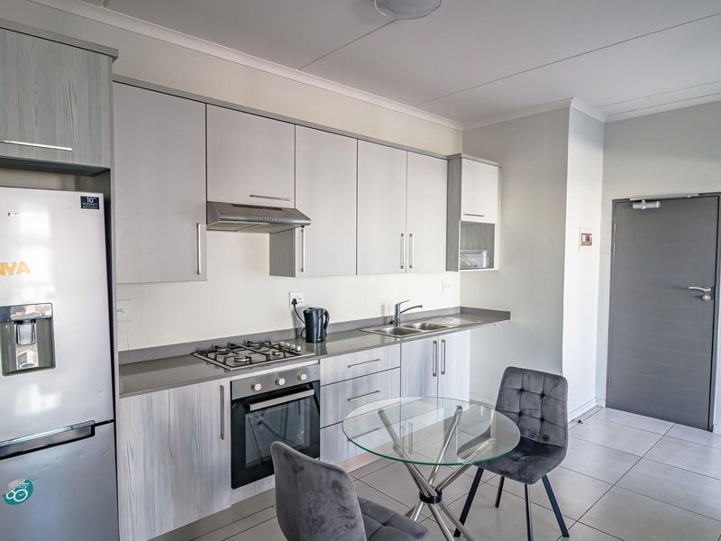 Modern kitchen featuring light wood-grain cabinetry, stone countertops, integrated gas hob, electric oven, and tiled flooring in a clean, well-maintained apartment setting.