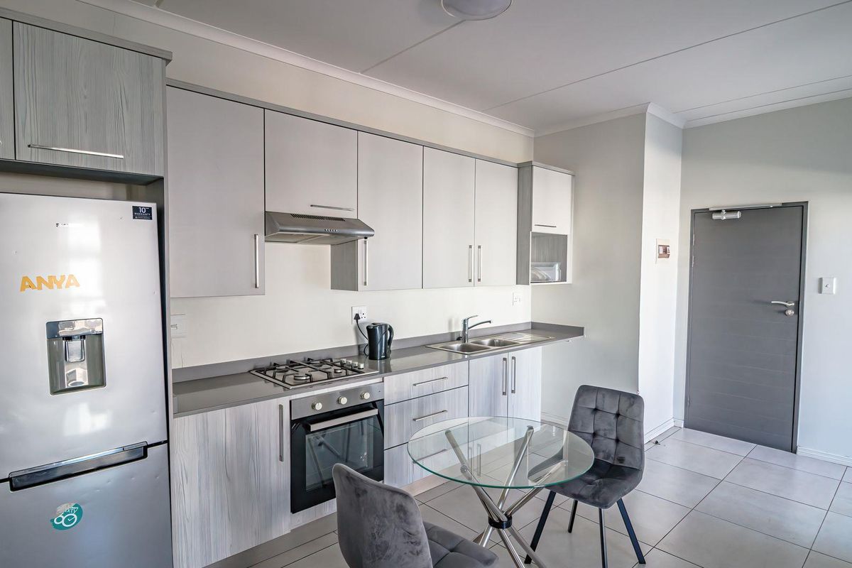 Modern kitchen featuring light wood-grain cabinetry, stone countertops, integrated gas hob, electric oven, and tiled flooring in a clean, well-maintained apartment setting.