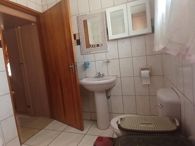 A dated bathroom featuring a pedestal basin, toilet, and full-height ceramic wall tiling. The space requires cosmetic updates to improve its overall condition.