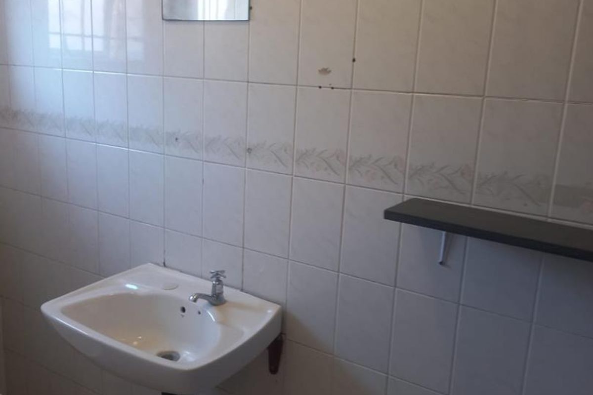 A basic bathroom wash area featuring a wall-mounted ceramic basin, tiled walls with decorative border, and a small wall-mounted shelf.