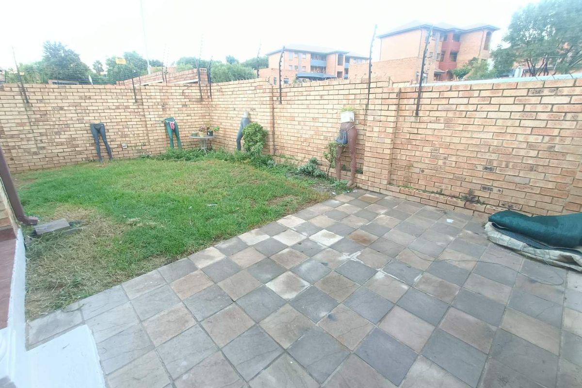 A private rear garden featuring a paved patio area and a small lawn, enclosed by high brick boundary walls with security fencing.