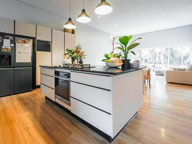 Modern open-plan kitchen featuring a central island with built-in oven and gas cooktop, complemented by sleek cabinetry and warm timber-look flooring.