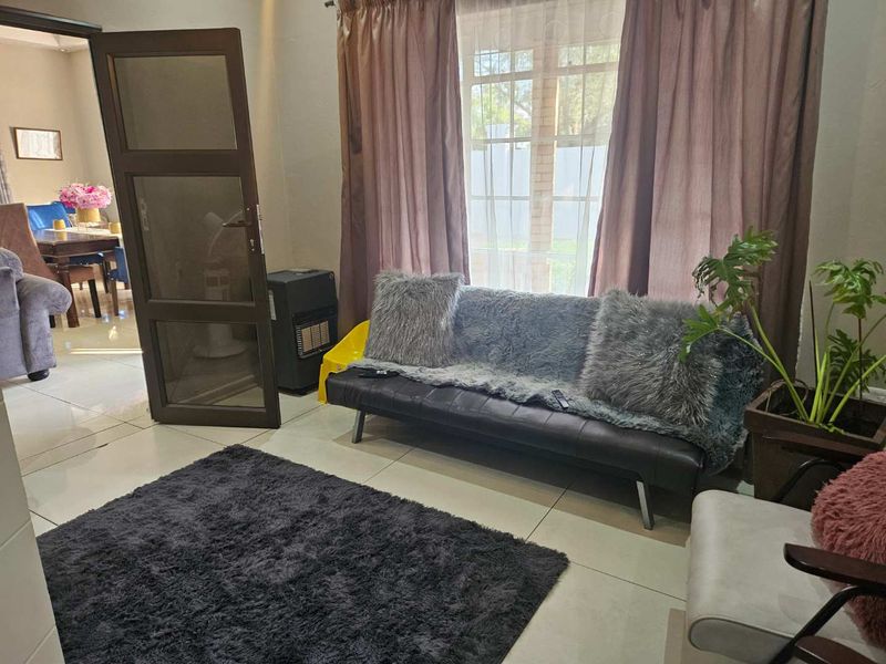 A living room area featuring tiled flooring and a timber-framed glass door leading to an adjacent space, with natural light from a large window.