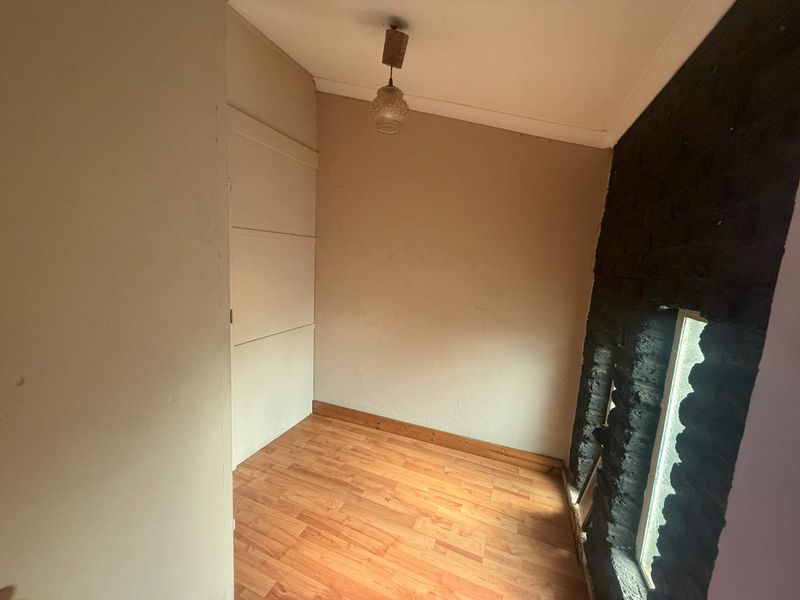 A small, empty bedroom featuring laminate wood flooring, a built-in closet, and a distinctive exposed brick wall section.
