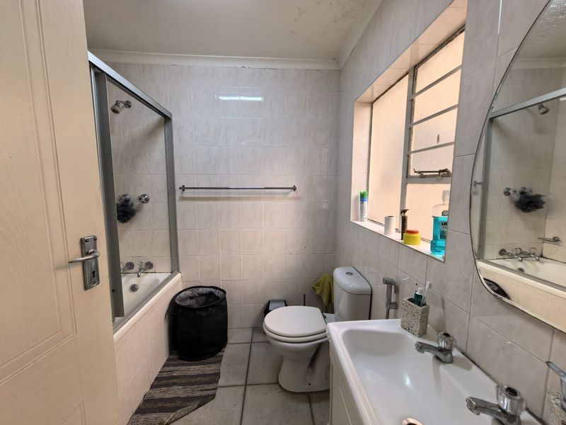 A functional bathroom featuring a bathtub with shower screen, toilet, and vanity basin, finished with tiled walls and flooring.