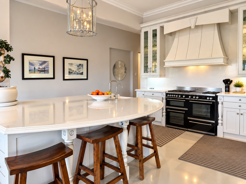 A bright, modern kitchen featuring a large central island with quartz countertops, high-end range cooker, custom cabinetry, and elegant pendant lighting.