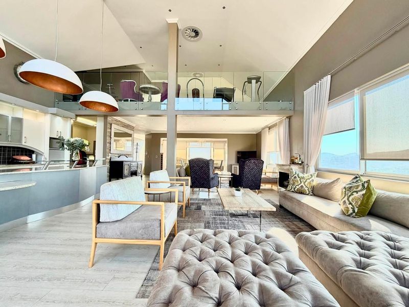 Spacious open-plan living area featuring a vaulted ceiling, mezzanine level with glass balustrade, and a modern kitchen with a curved island and stone countertops.