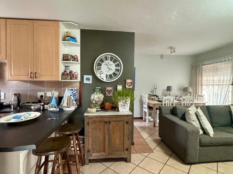 Open-plan living area featuring a kitchen with laminate cabinetry and breakfast bar, flowing into a dining and lounge space with tiled flooring.