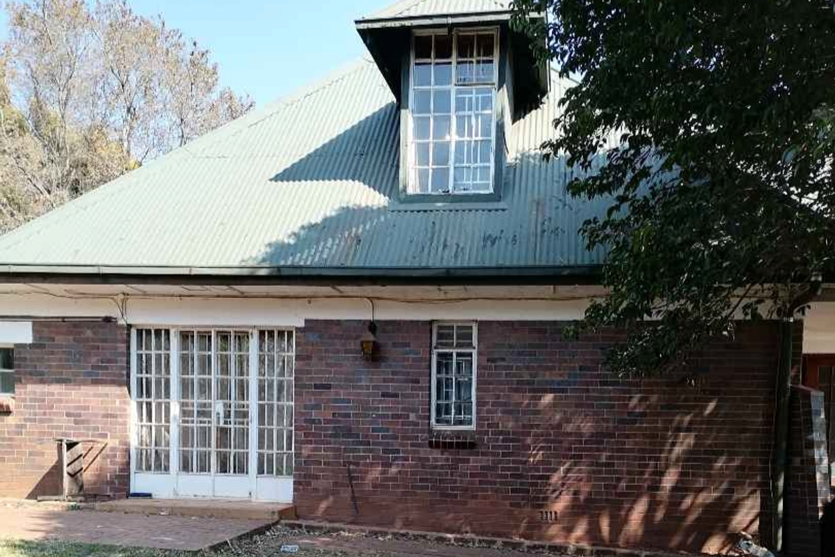 Rear view of a brick house featuring a corrugated metal roof, a prominent dormer window, and a paved patio area with french door access.
