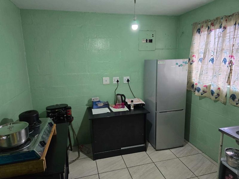 A basic kitchen area featuring tiled flooring and painted blockwork walls, requiring significant cosmetic updates and improved cabinetry to enhance functionality.