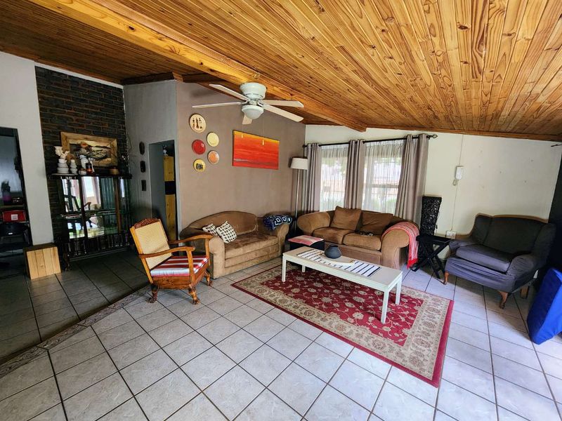 Spacious living room featuring a distinctive exposed timber ceiling, ceramic tiled flooring, and an exposed brick fireplace feature wall.