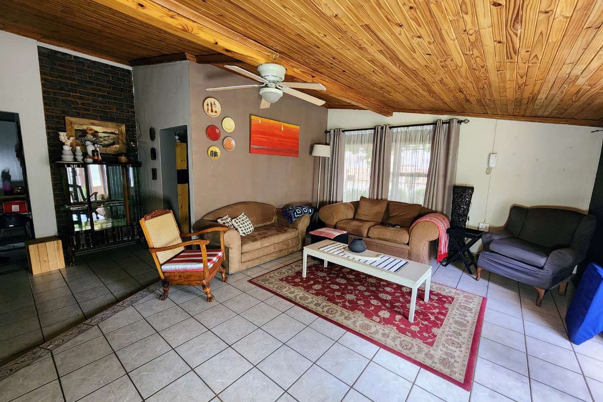 Spacious living room featuring a distinctive exposed timber ceiling, ceramic tiled flooring, and an exposed brick fireplace feature wall.