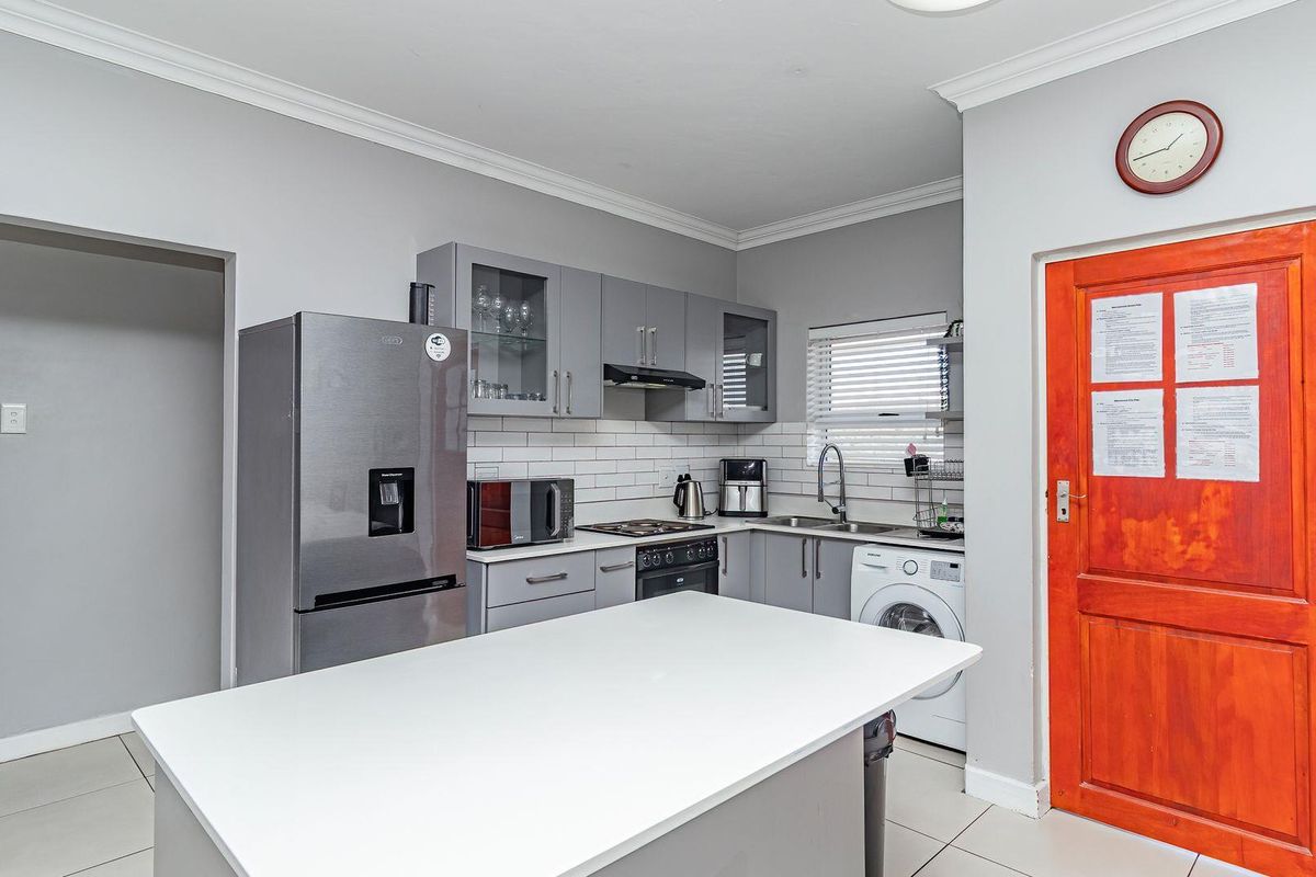 Modern kitchen featuring grey cabinetry, subway tile backsplash, built-in oven and hob, and a central island with a white countertop.