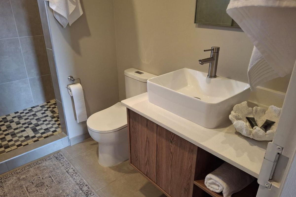 Modern bathroom featuring a vessel sink on a wood-finish vanity, a sleek toilet, and a walk-in shower with mosaic floor tiling.