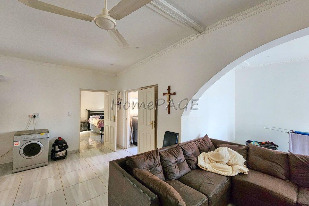 A living area featuring tiled flooring, a ceiling fan, and decorative crown molding, with access to adjacent rooms.