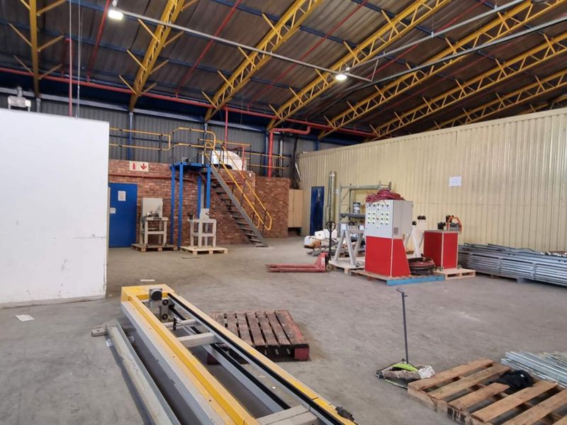 Spacious industrial warehouse featuring high-clearance steel truss roofing, concrete flooring, and integrated mezzanine access with metal staircase.
