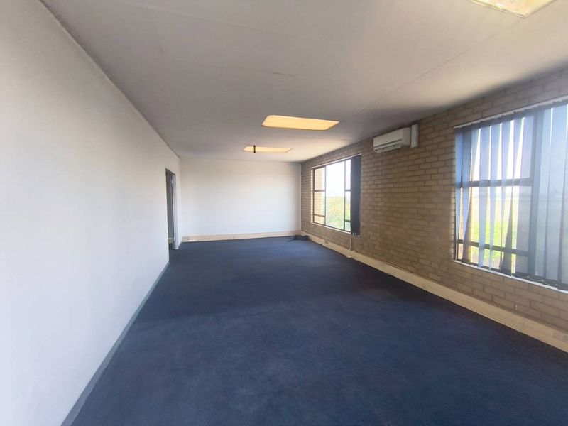 A spacious, empty office area featuring exposed brick walls, recessed lighting, and an integrated air conditioning unit, suitable for a professional workspace.