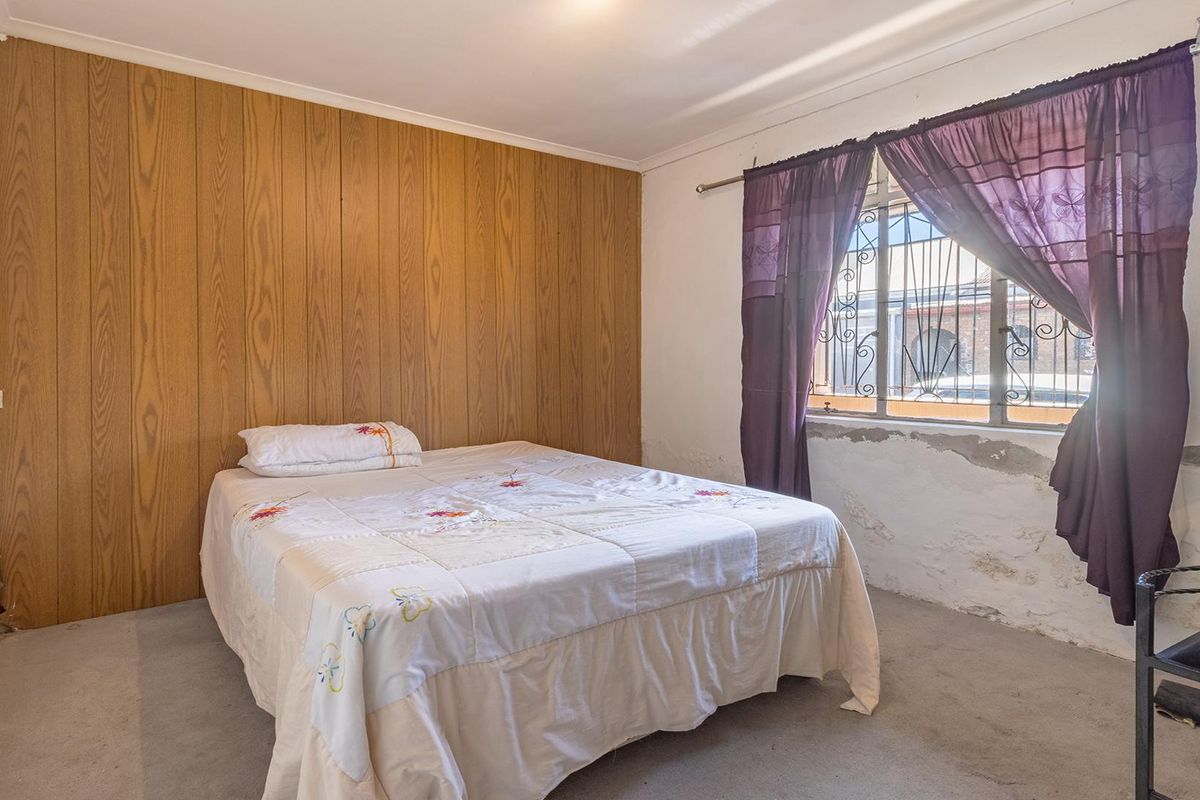 Bedroom featuring wood paneling, carpet flooring, and security bars on the window, requiring cosmetic attention to the wall finishes.