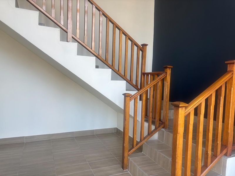 A bright entrance area featuring a wooden staircase with a matching balustrade and neutral tiled flooring.