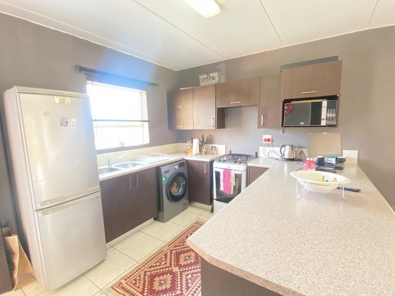 A functional kitchen featuring dark laminate cabinetry, stone-look countertops, a gas stove, and integrated microwave, with tiled flooring and natural light.
