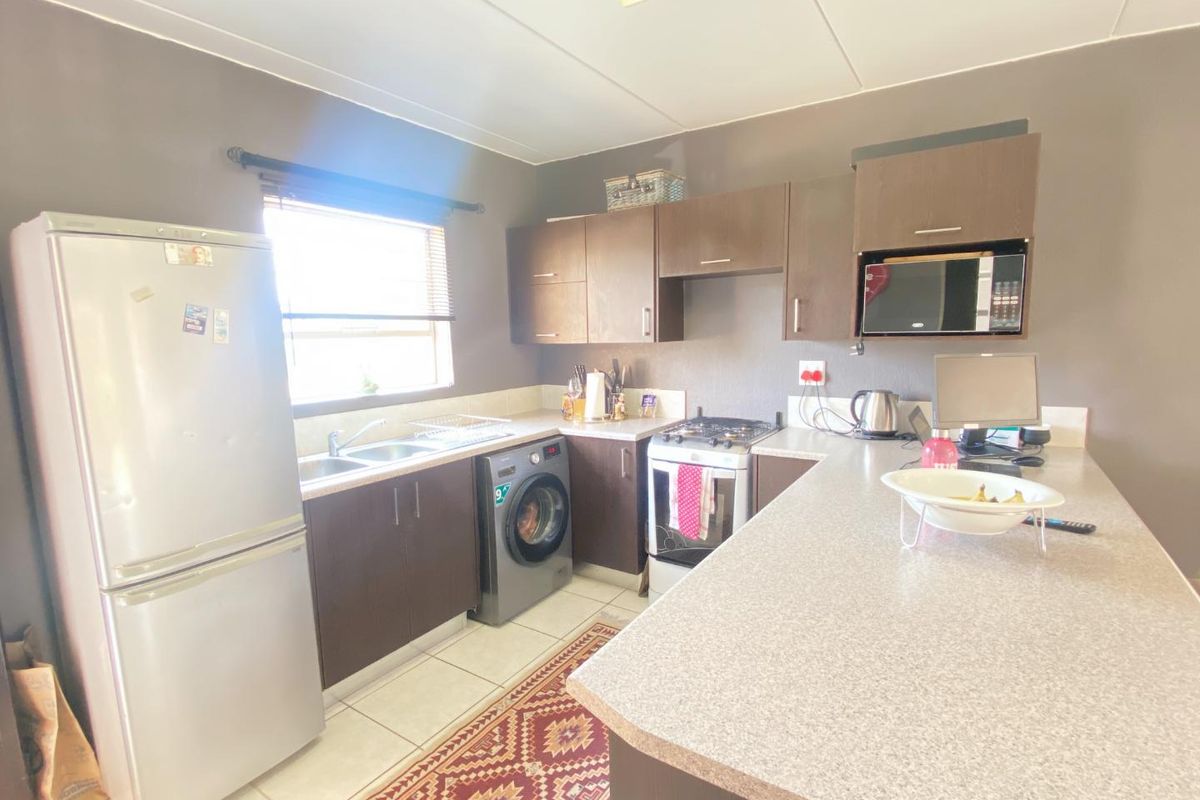 A functional kitchen featuring dark laminate cabinetry, stone-look countertops, a gas stove, and integrated microwave, with tiled flooring and natural light.