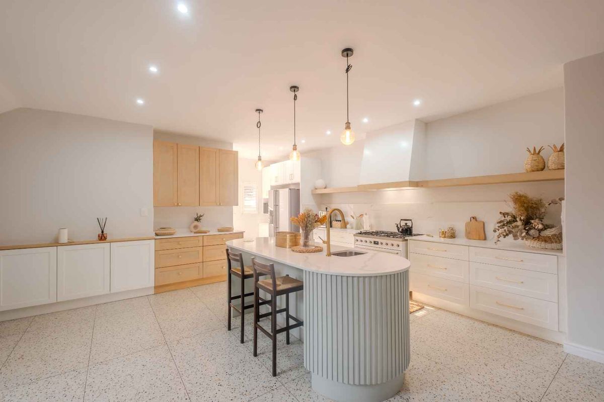 Modern kitchen featuring a central island with a curved base, light wood cabinetry, stone countertops, integrated gas cooktop, and stylish pendant lighting.