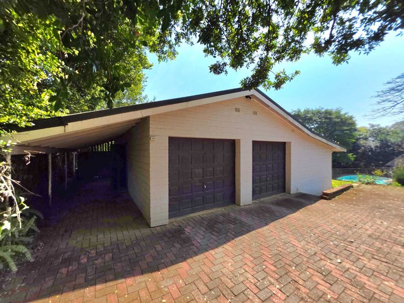 A detached double garage featuring two garage doors and an adjacent covered carport area, set on a brick-paved driveway.