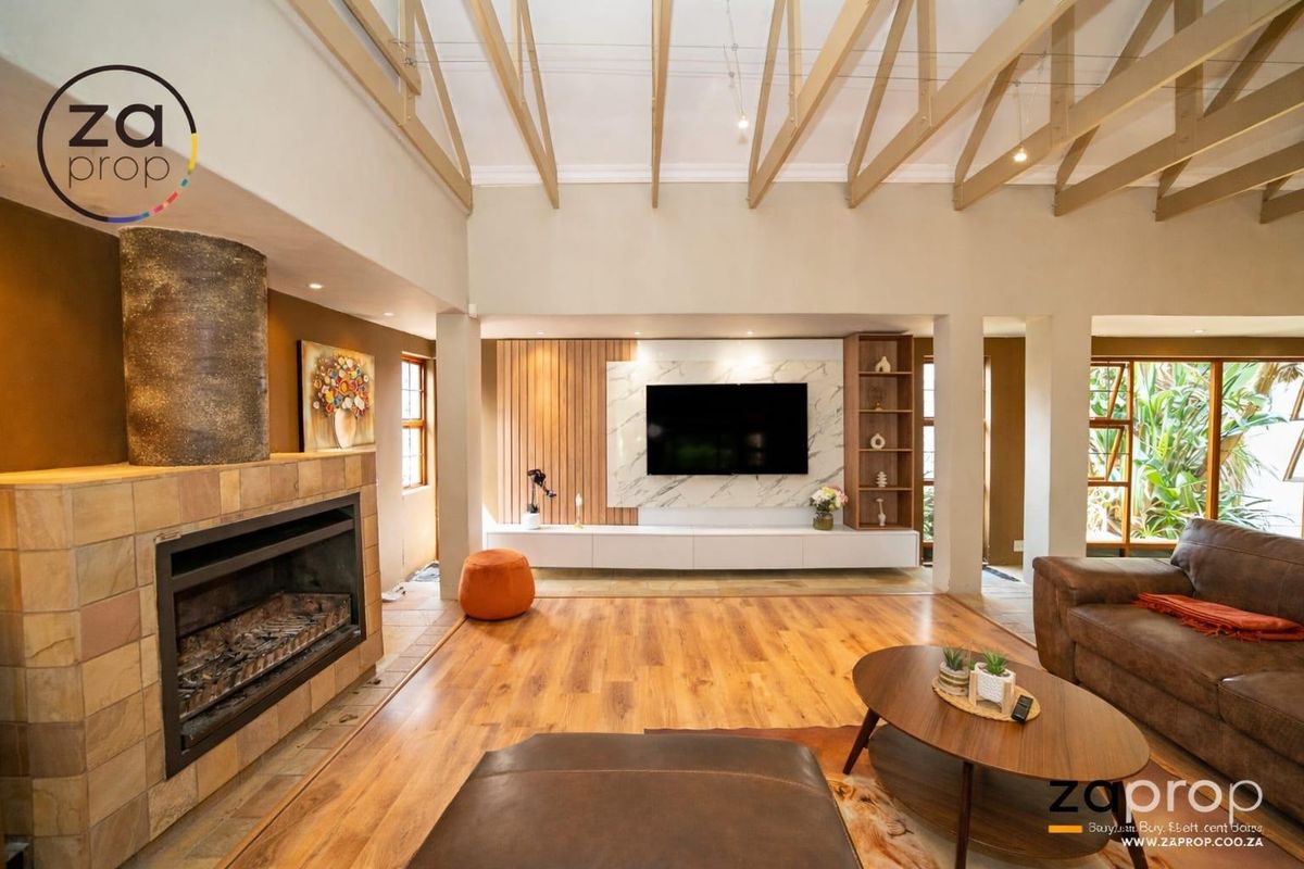 Spacious living room featuring high vaulted ceilings with exposed timber beams, a stone-clad fireplace, and a modern built-in media wall with shelving.