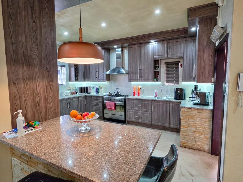 Modern kitchen featuring wood-grain cabinetry, granite countertops, a stone-clad breakfast bar, and stainless steel appliances with integrated under-cabinet lighting.