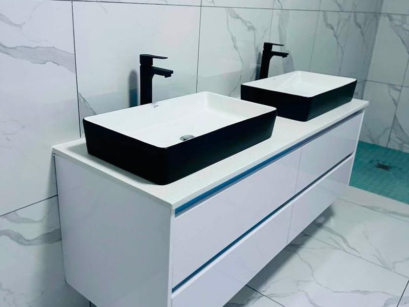 Modern bathroom featuring a sleek double vanity with vessel sinks, matte black fixtures, and contemporary marble-look tiling throughout.