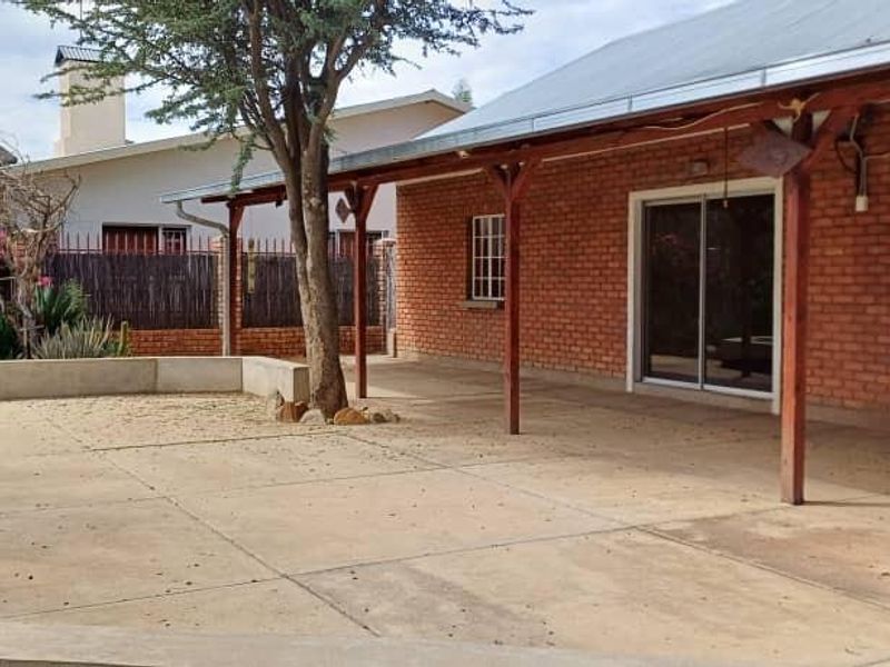 A spacious outdoor patio area featuring exposed brick walls, a timber pergola, and concrete flooring, providing a functional space for outdoor living.