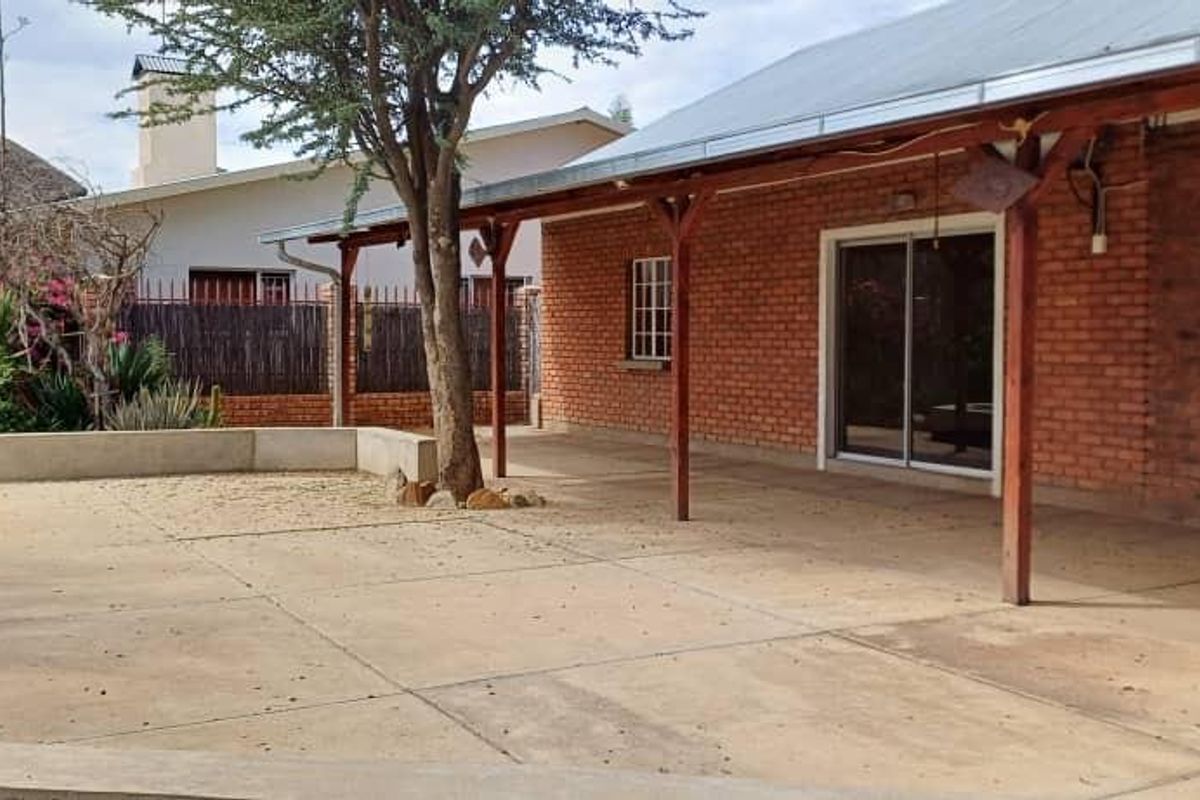 A spacious outdoor patio area featuring exposed brick walls, a timber pergola, and concrete flooring, providing a functional space for outdoor living.