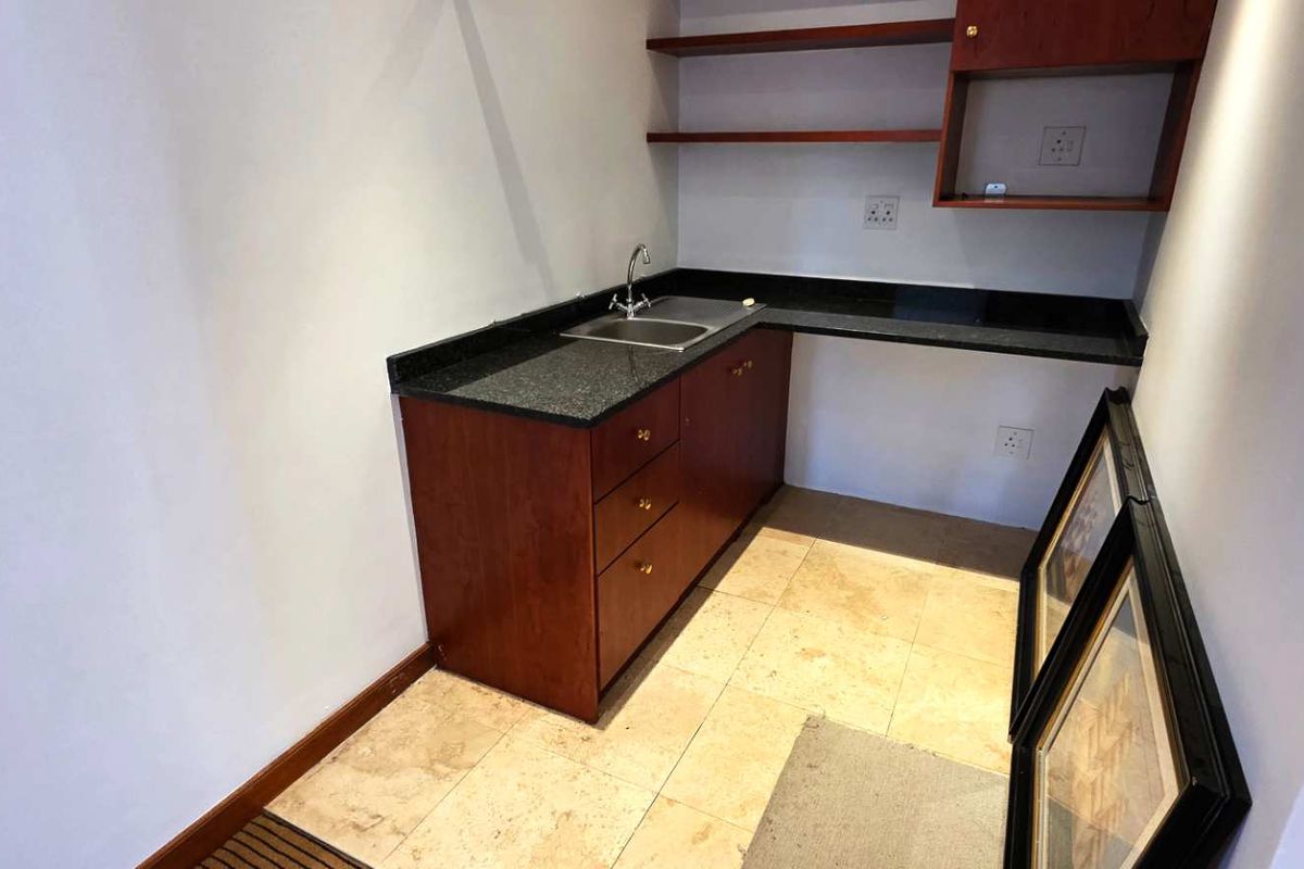 A compact kitchenette area featuring dark wood cabinetry, granite countertops, a stainless steel sink, and open shelving.