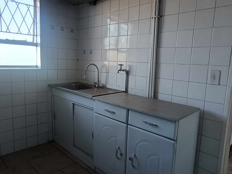 A functional laundry area featuring a stainless steel sink, built-in cabinetry, and tiled wall finishes, providing a practical utility space.