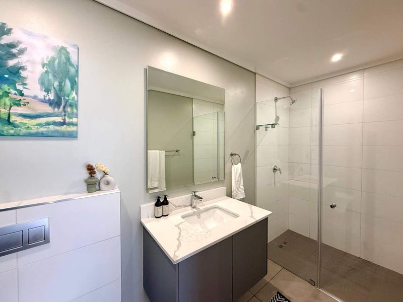 Modern bathroom featuring a wall-mounted toilet, vanity with stone countertop, and a spacious walk-in shower with a glass screen.