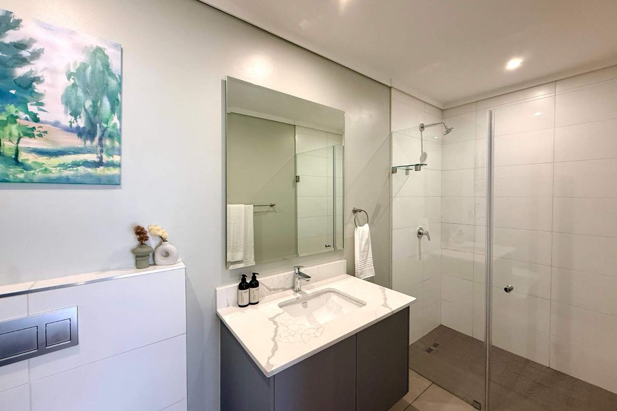 Modern bathroom featuring a wall-mounted toilet, vanity with stone countertop, and a spacious walk-in shower with a glass screen.