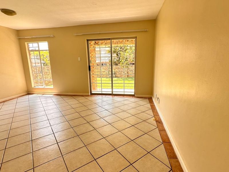 Spacious, empty living room featuring neutral tiled flooring, large windows with security bars, and a sliding glass door providing access to the rear garden.