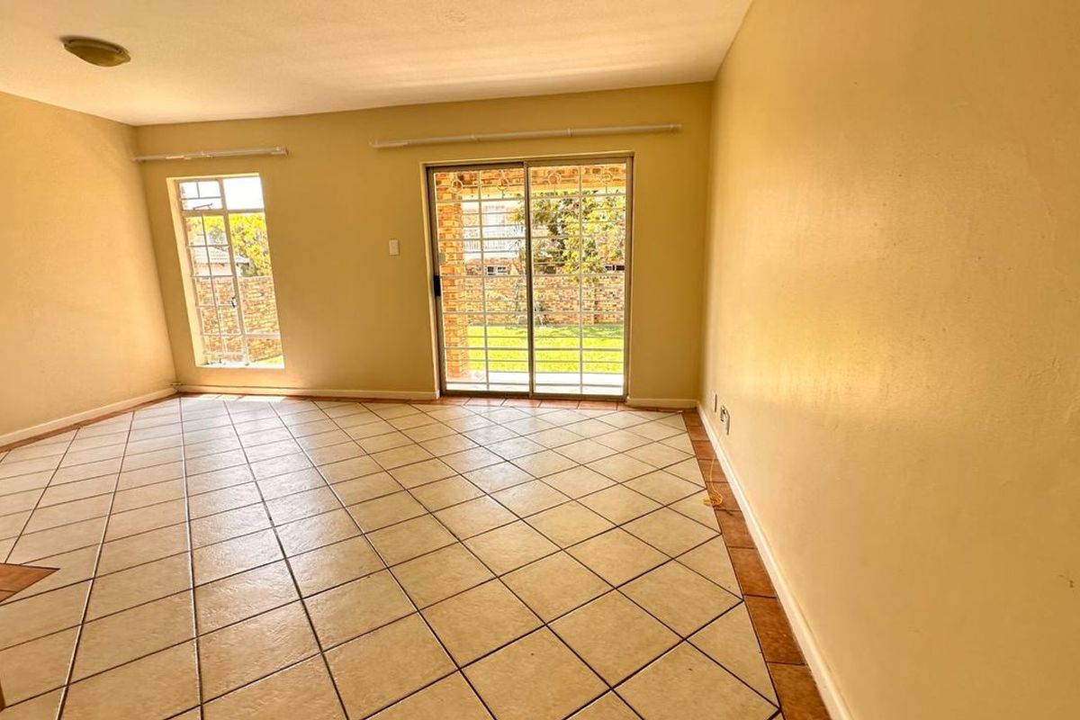 Spacious, empty living room featuring neutral tiled flooring, large windows with security bars, and a sliding glass door providing access to the rear garden.