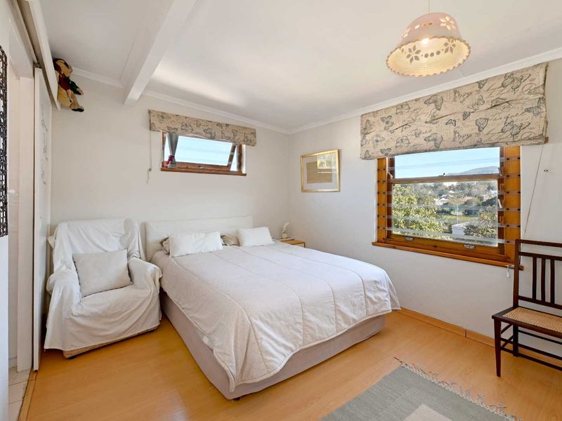 A well-lit bedroom featuring laminate flooring, timber-framed windows with views, and built-in wardrobe storage.