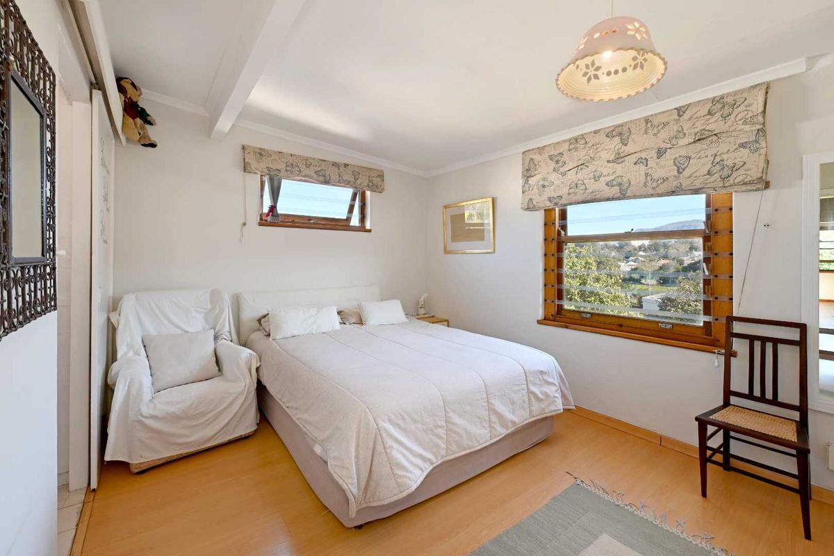 A well-lit bedroom featuring laminate flooring, timber-framed windows with views, and built-in wardrobe storage.