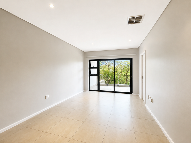 A bright, empty bedroom featuring neutral tiled flooring, recessed lighting, and a large sliding glass door providing access to an outdoor balcony.