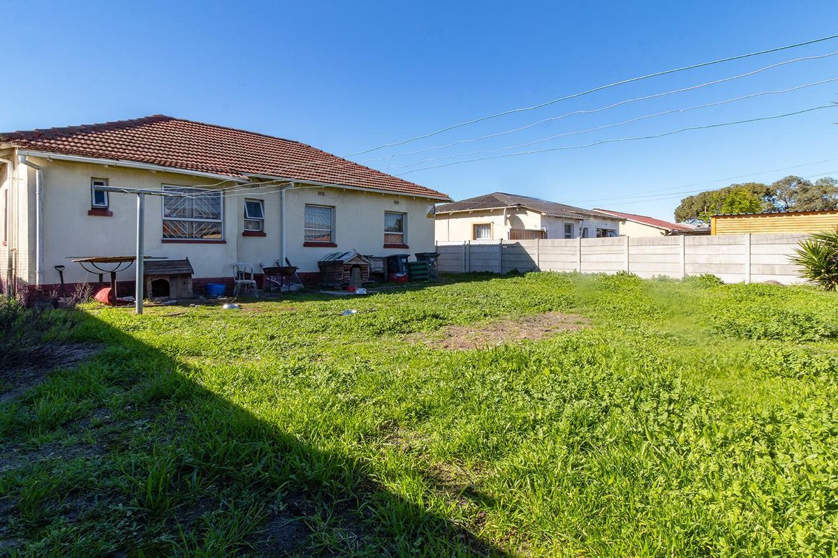 Rear view of the house featuring a tiled roof, security bars on windows, and a large, unmaintained garden area enclosed by a precast concrete wall.