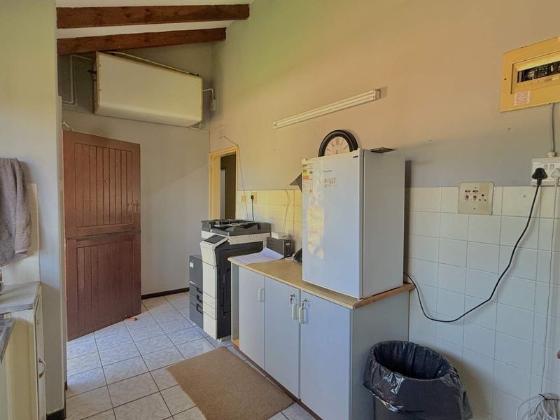 A functional kitchen area featuring tiled flooring, a tiled splashback, and exposed timber ceiling beams, offering potential for modernization and layout optimization.