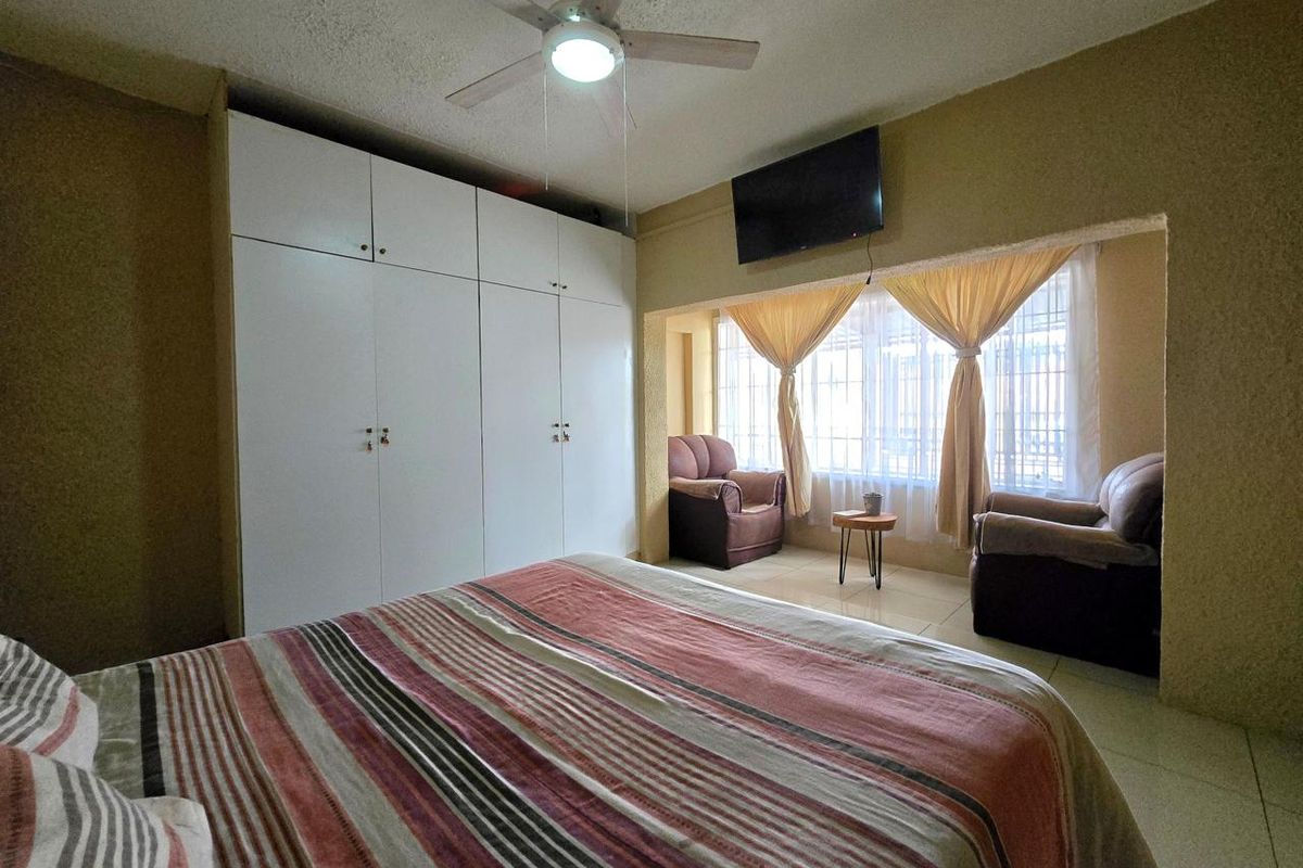 A bedroom featuring built-in floor-to-ceiling wardrobes, a ceiling fan, and a recessed window area with tiled flooring.
